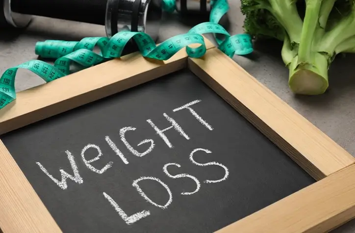 Weight Loss written on a board with a measuring tape nearby to illustrate the weight loss program offered at our Santa Rosa spa